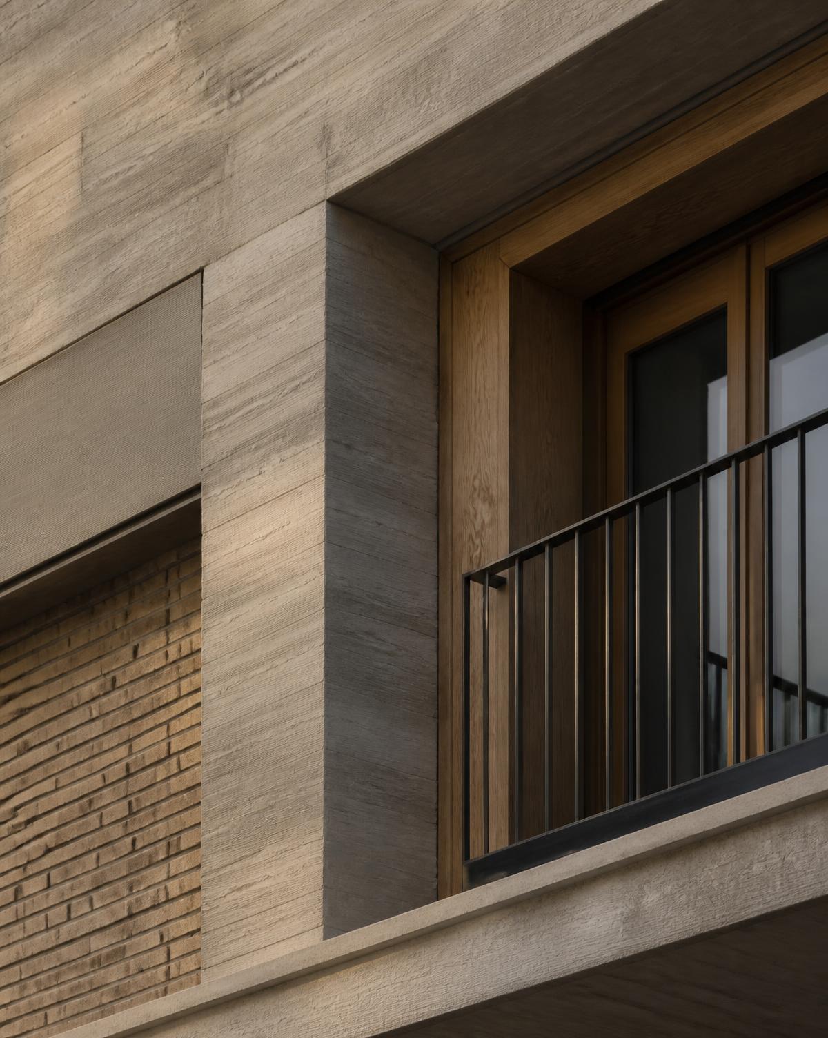 Detail van een woongebouw: beton, baksteen en een houten kozijn met balkonhek